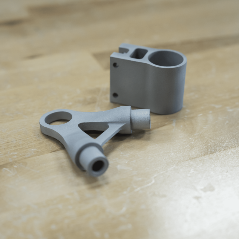 Two metal brackets 3D printed with DMLS resting on a workbench