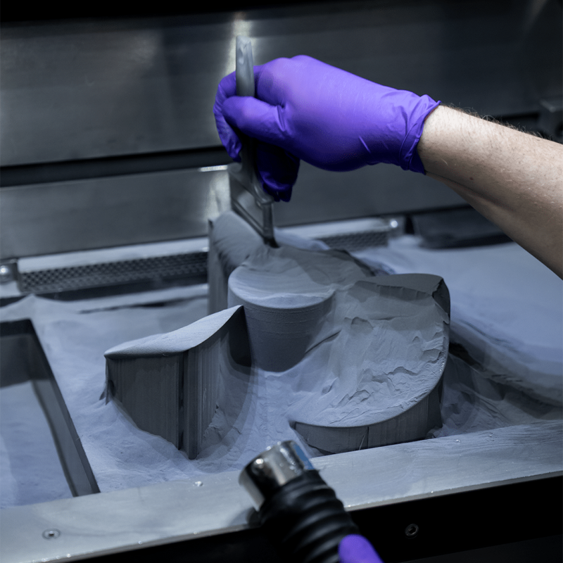 A technician brushing loose powder away from finished metal parts in the DMLS powder bed