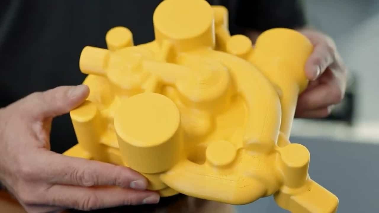 Hands holding a large yellow FDM-printed pump housing at Evology Manufacturing