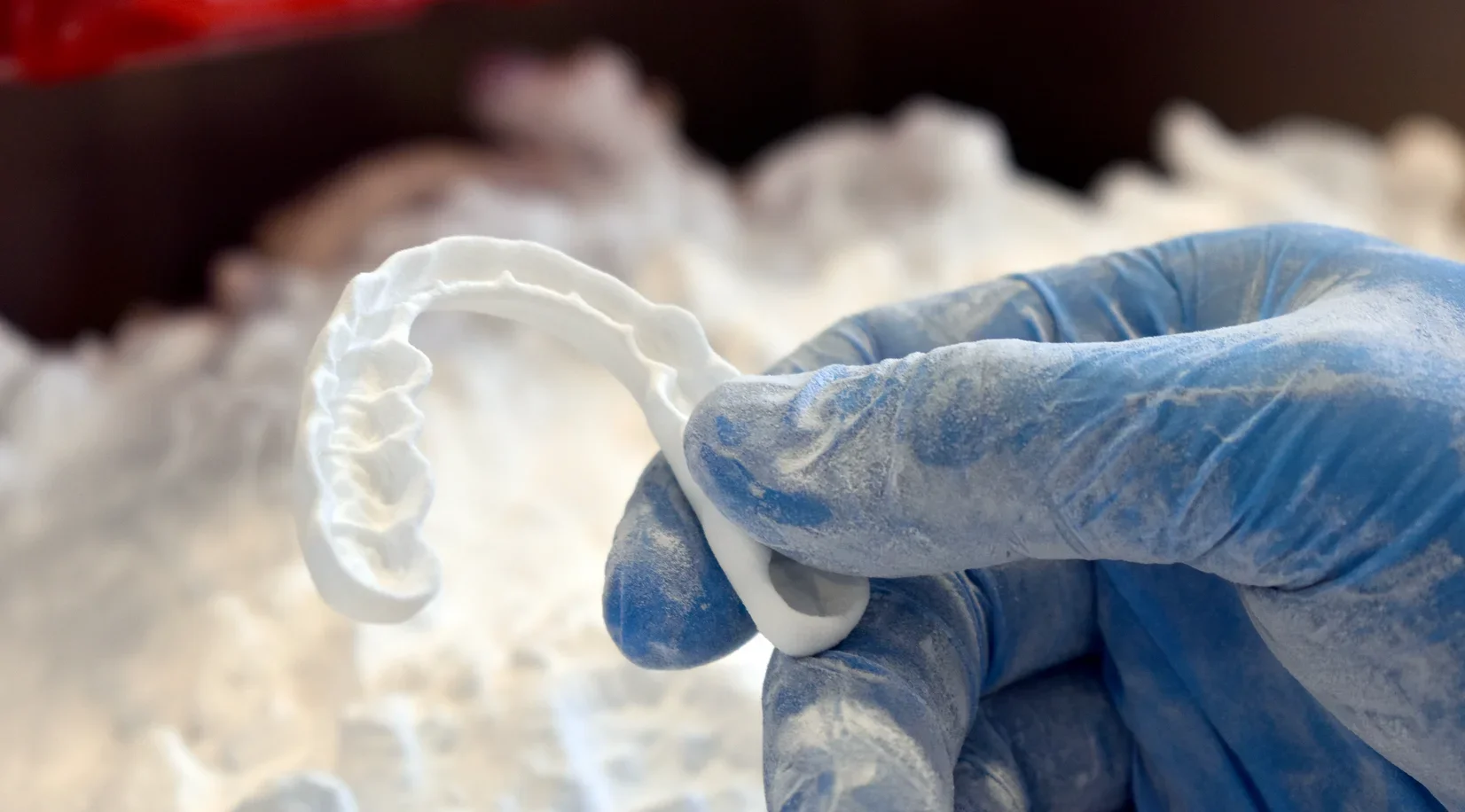 Gloved hand lifting an SLS-printed dental splint out of unfused nylon powder