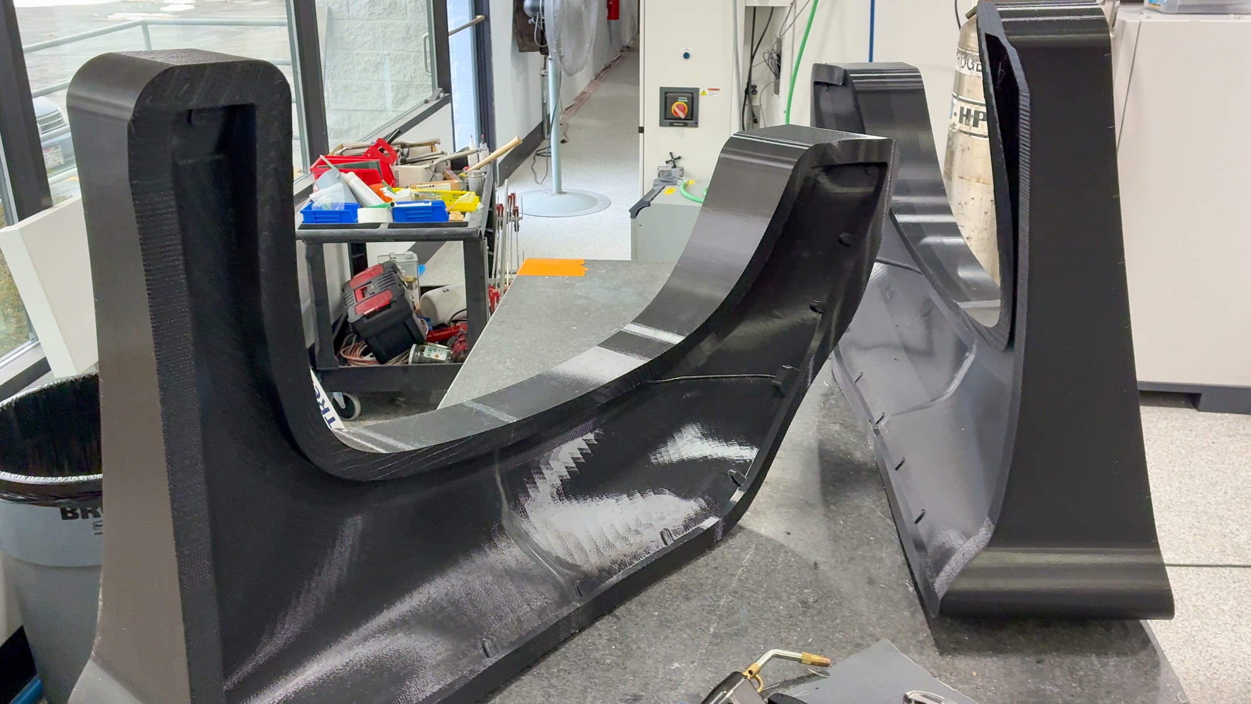 Two large black FDM-printed ASA carbon fiber layup molds with a curved profile on the shop floor