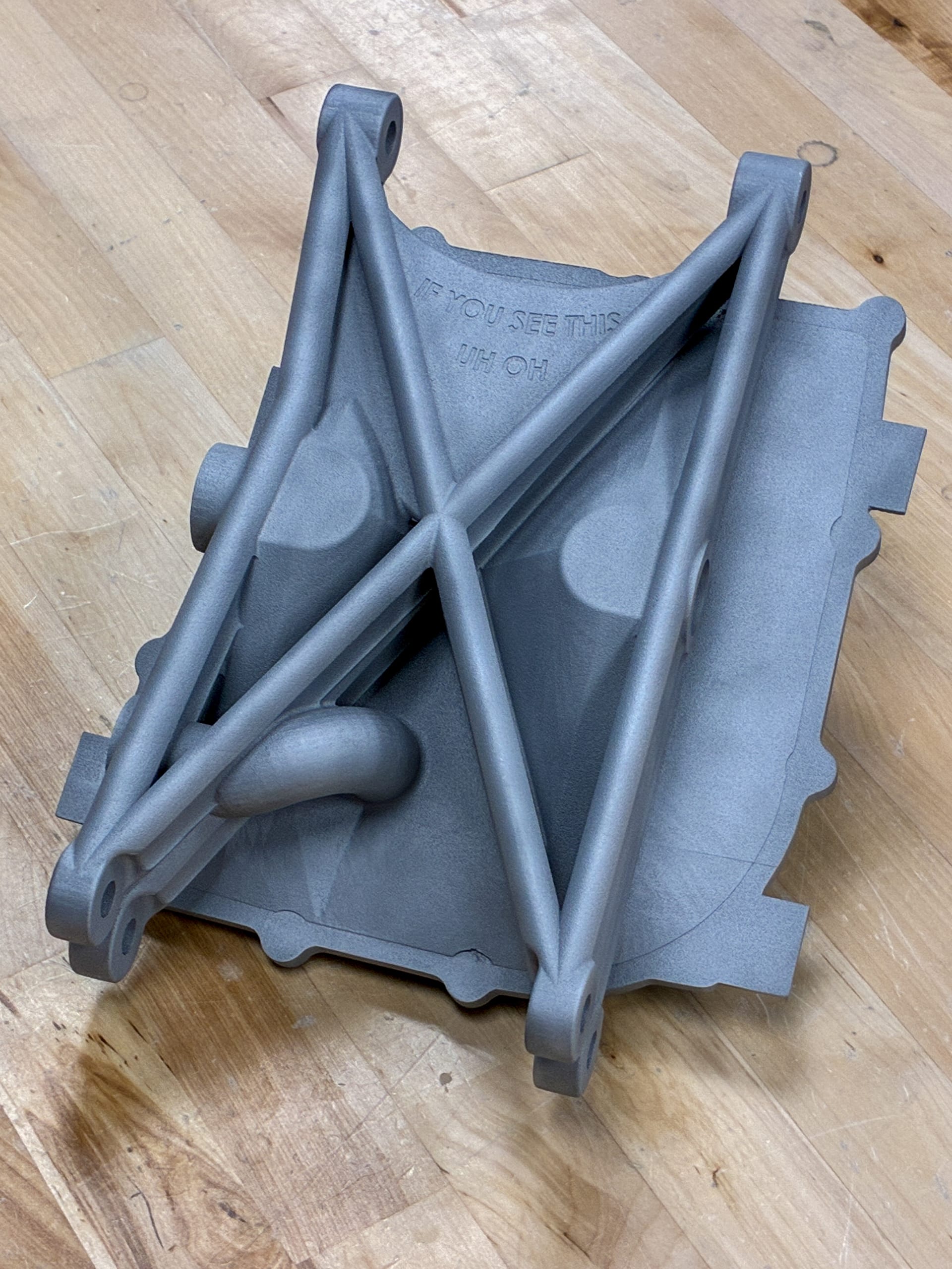 The as-printed PR26 DMLS oil pan showing its structural X-bracing, resting on a workbench